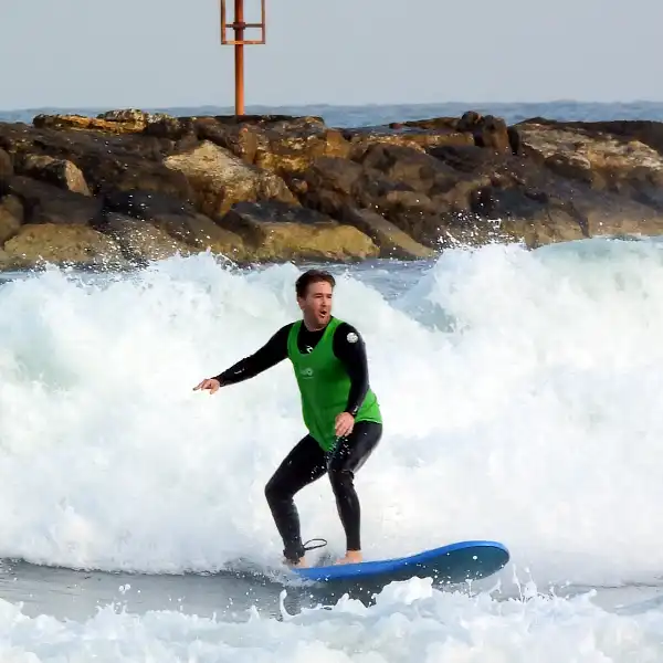 גולש בגופייה ירוקה נעמד על גלשן בגל ליד שובר הגלים
